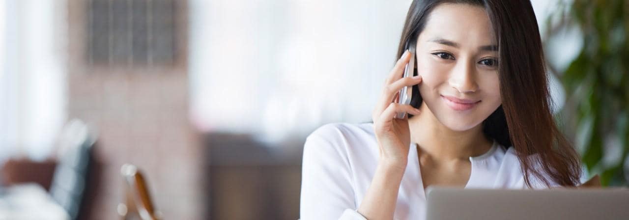 Young business woman at desktop computer and on mobile phone