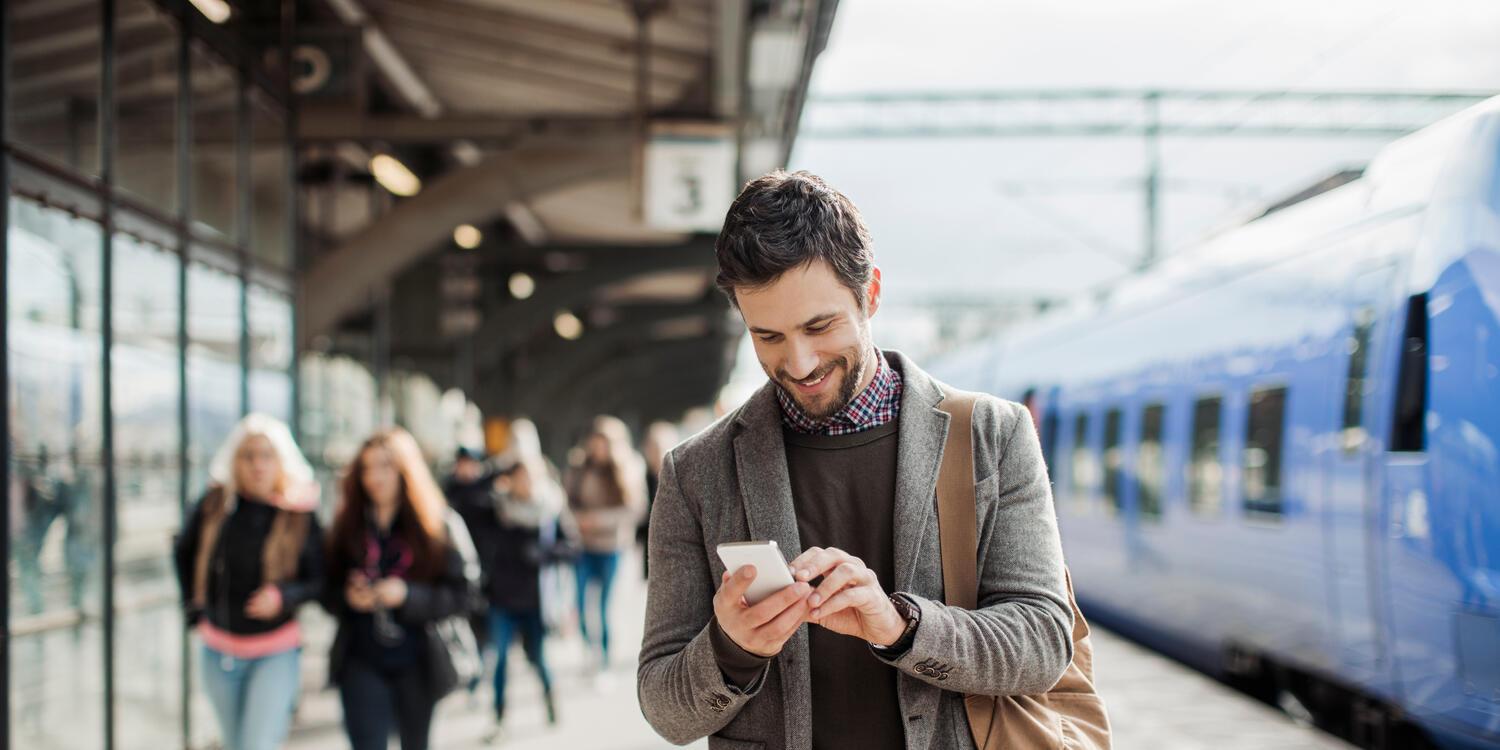 Smiling businessman texting on his mobile phone at a train station
