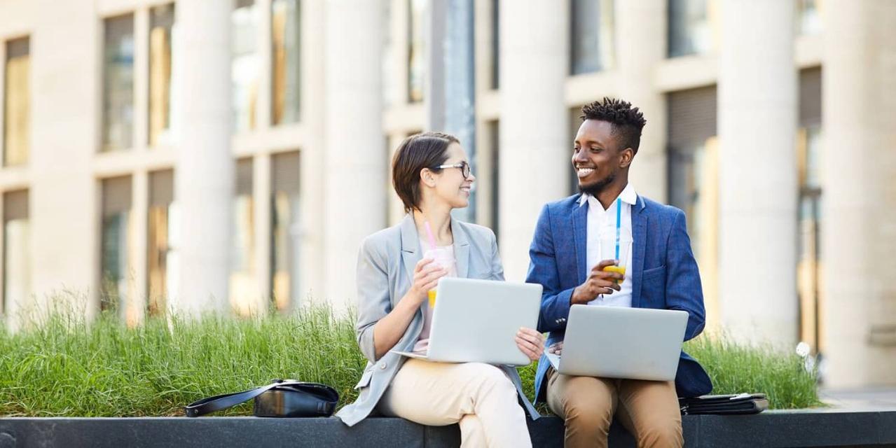 Two happy professionals sitting outside with laptops