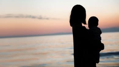 A silhouette of baby and mother looking at the ocean in the sunset