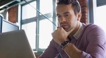 Pensive man working on a laptop surrounded by monitors