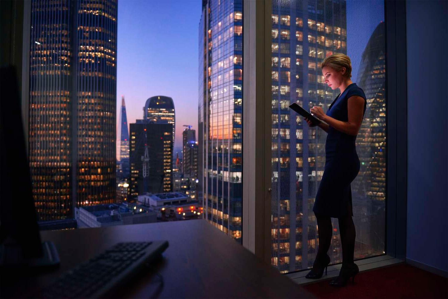Blond woman on tablet in front of cityscape