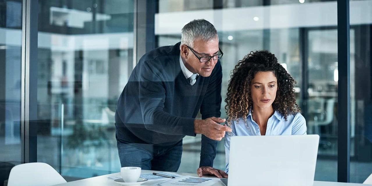 Two coworkers with laptop in office with glass walls