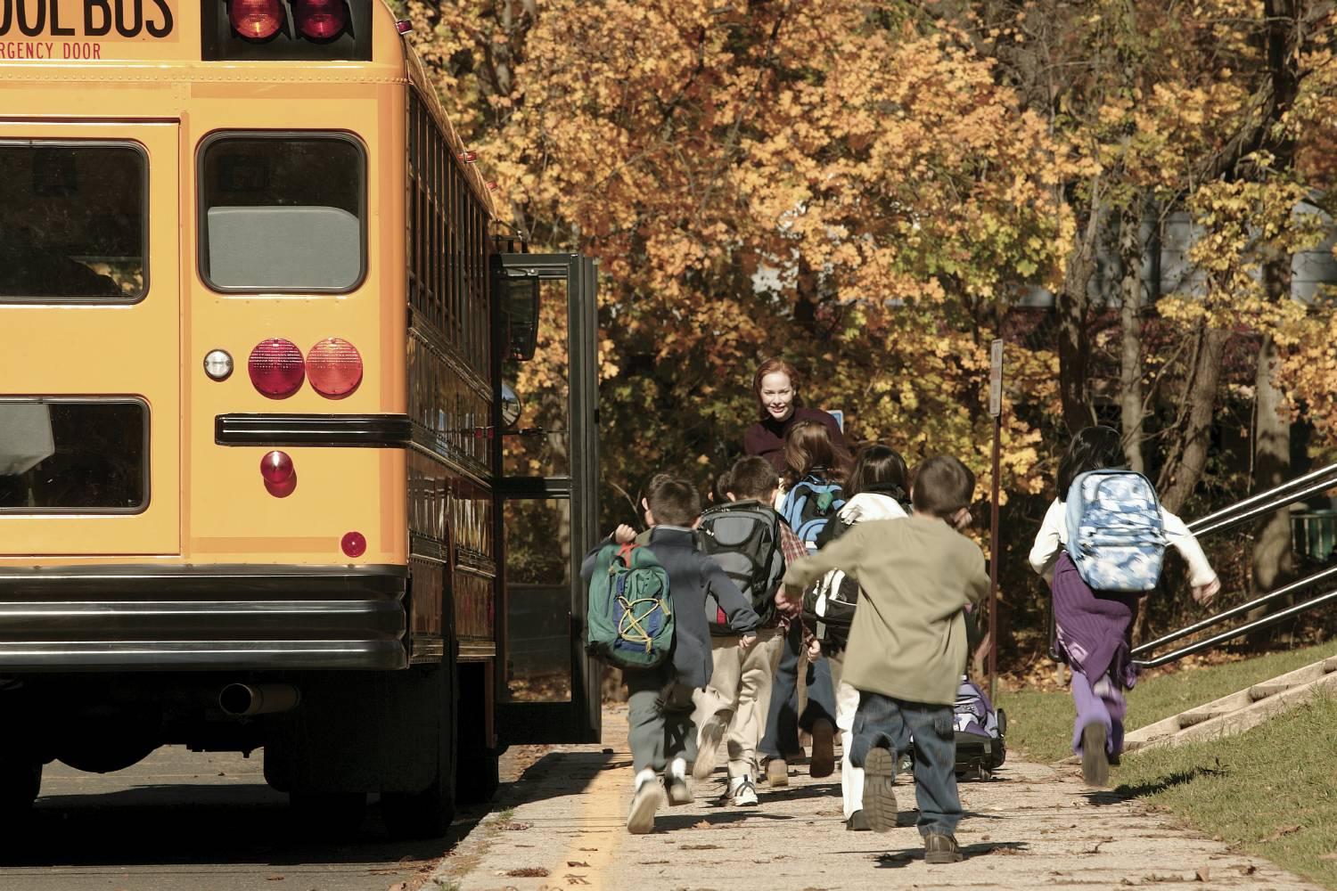 Kids getting on a school bus with a teachers help