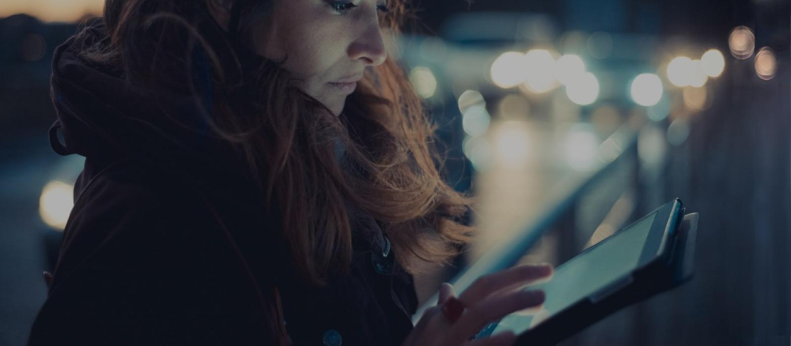 Mid adult woman using digital tablet touchscreen on street at dusk