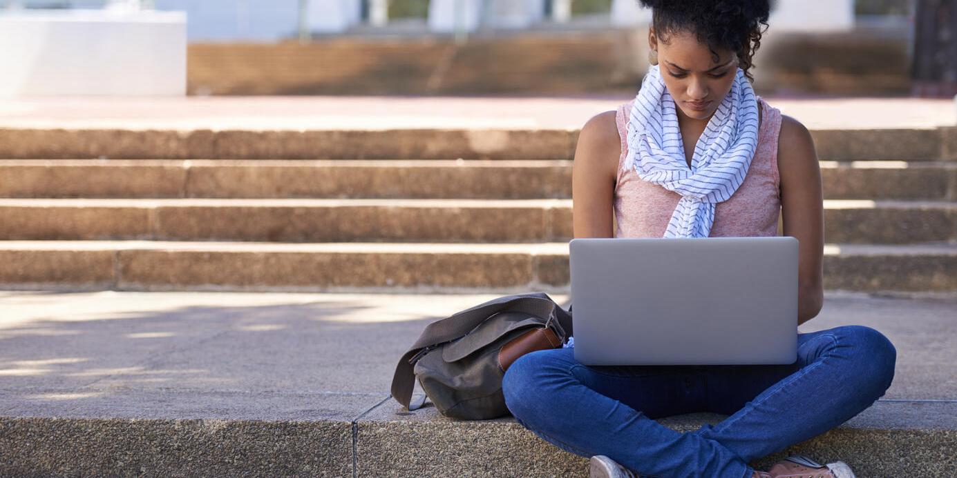 Woman sitting on the steps of her college doing research on her laptop