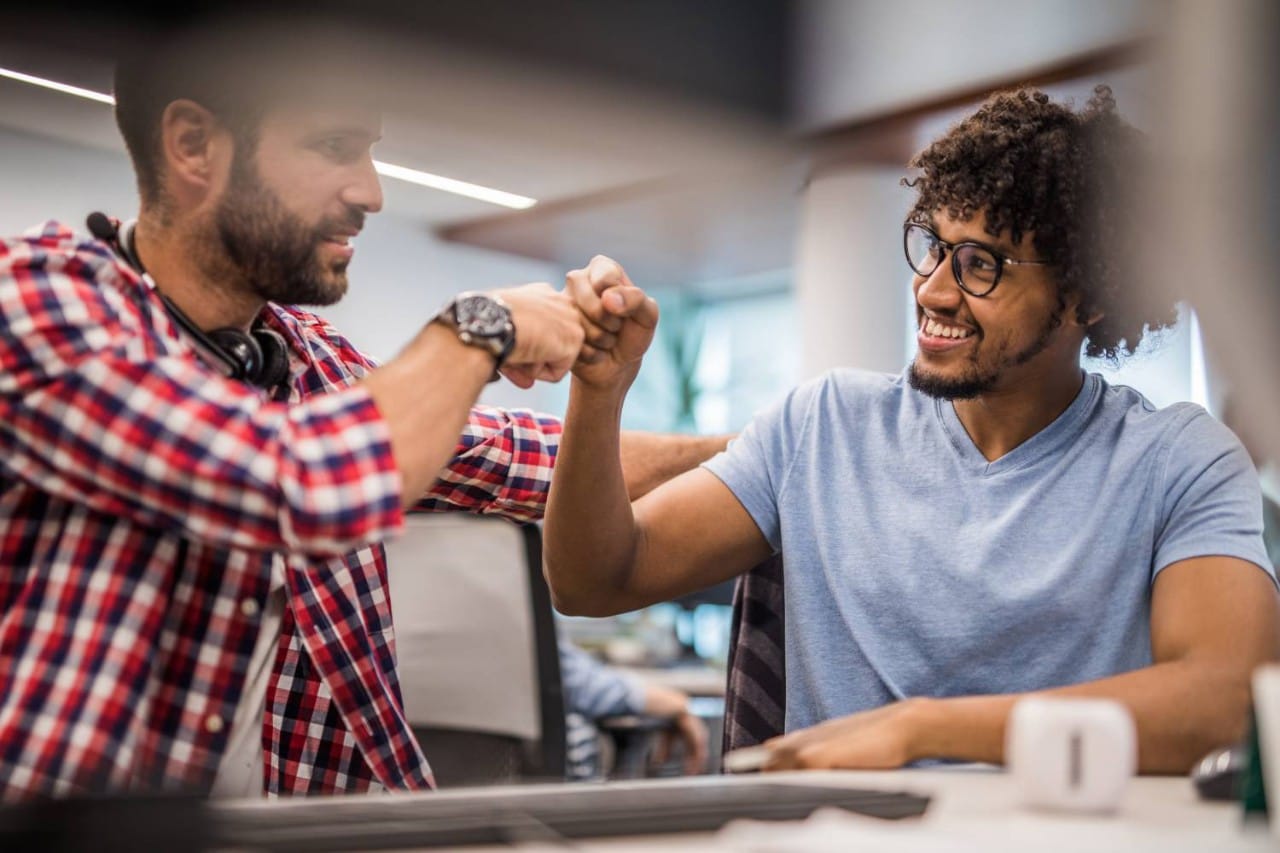 Two males in an office setting fist bumping in celebration