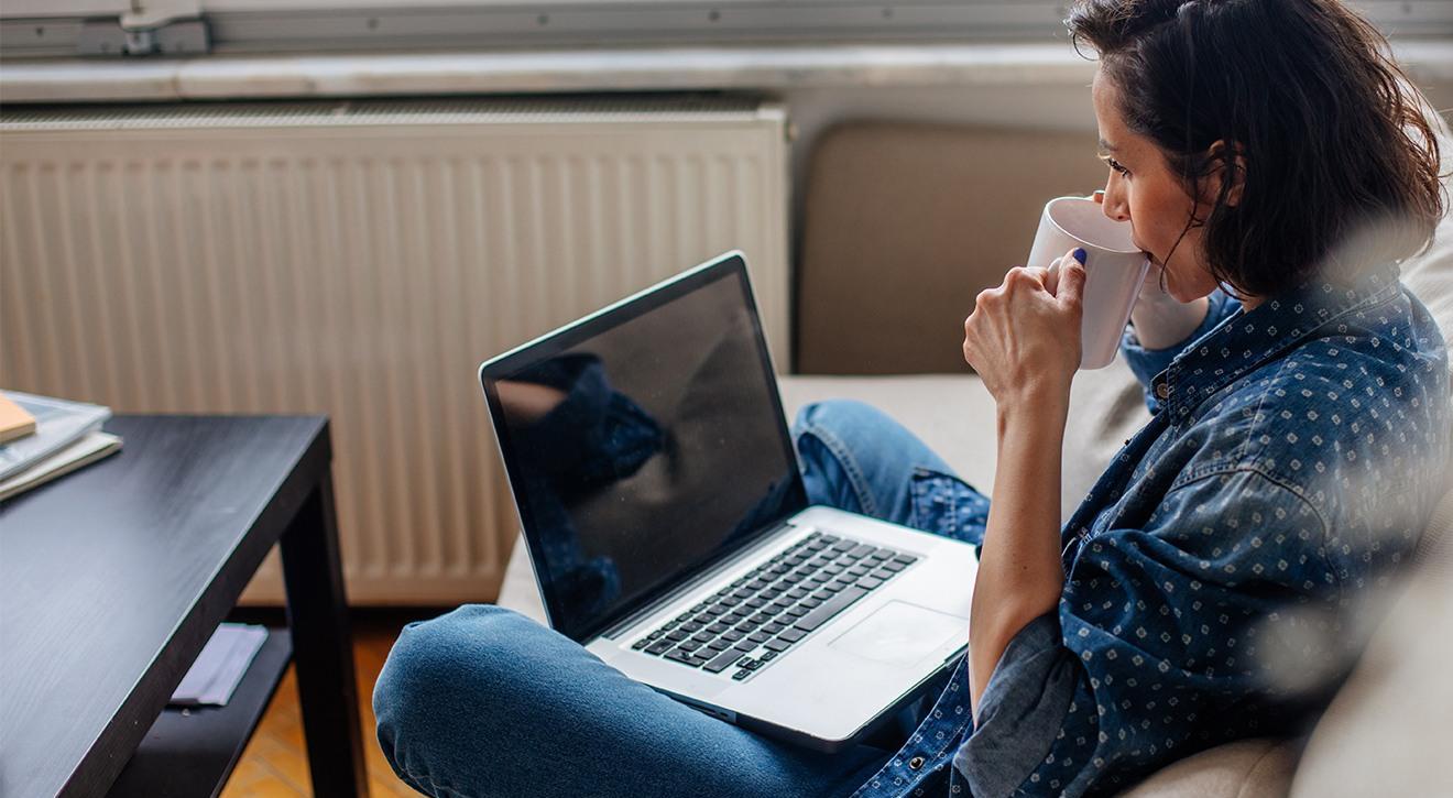 Woman drinking coffee and using a laptop in home