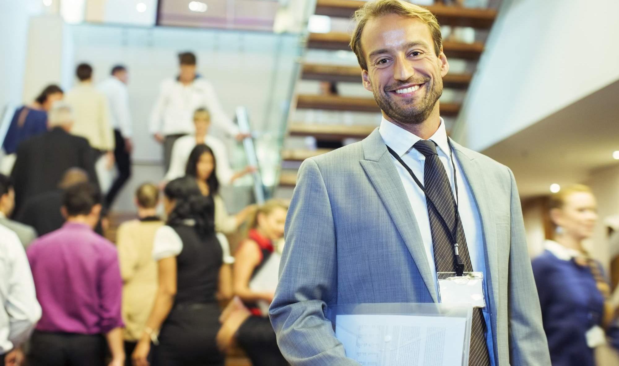 Portrait of smiling businessman standing in crowded lobby of conference center