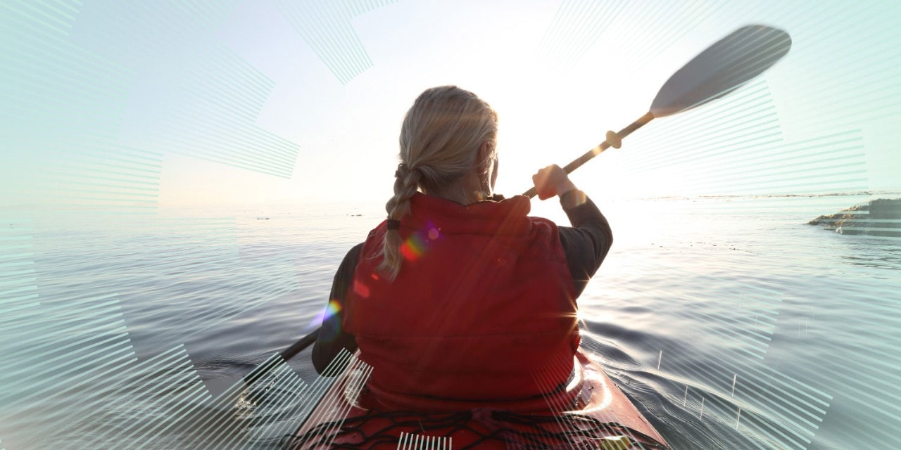 Woman paddles kayak on calm sea, towards sunrise