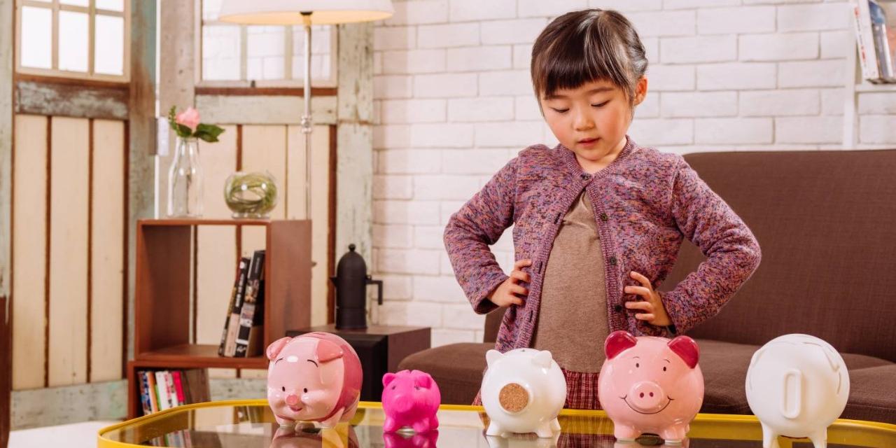Little girl thinking in front of piggy banks