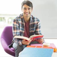 Smiling male student with book in purple chair