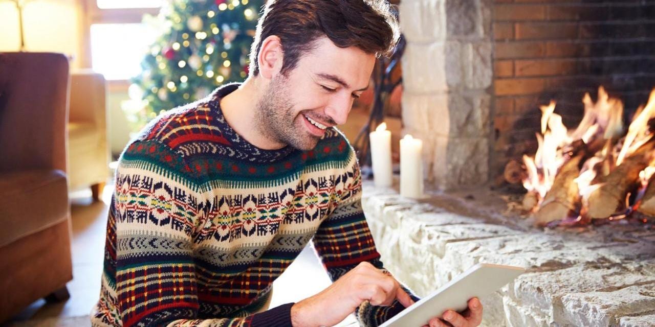 Man in winter sitting in front of a fireplace with iPad, christmas tree in the back
