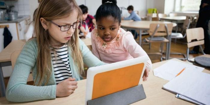 Two young female students use tablet device in classroom
