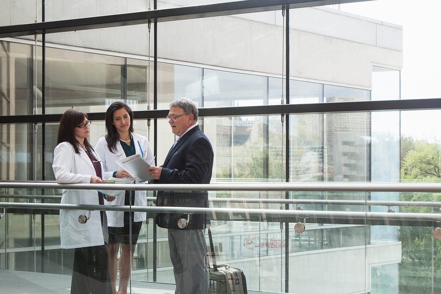Male pharmaceutical representative with two female doctors looking at paperwork in medical facility skywalk area