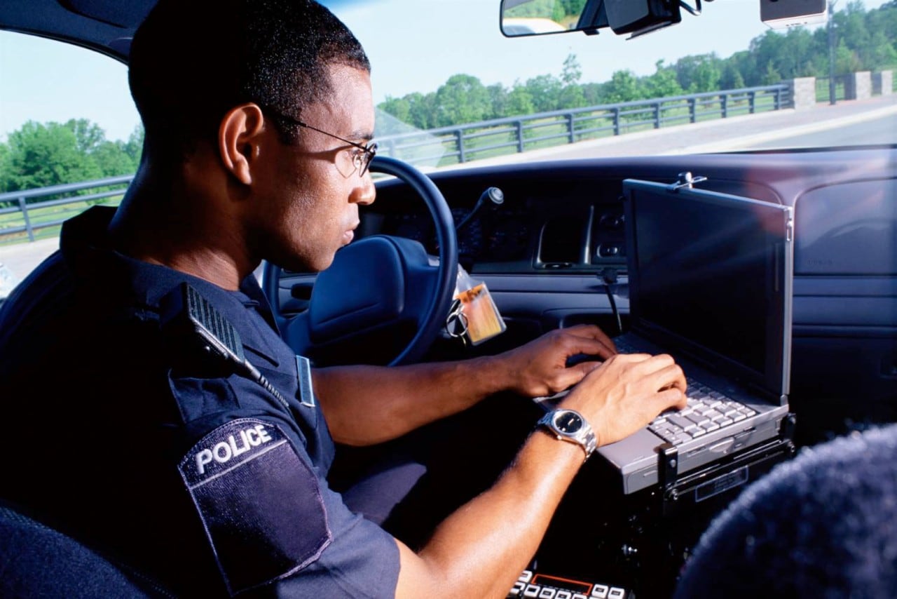 police officer parked in car on laptop
