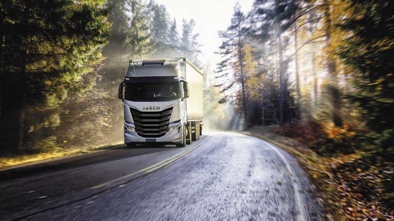 Iveco Group truck drives on tree-lined highway.