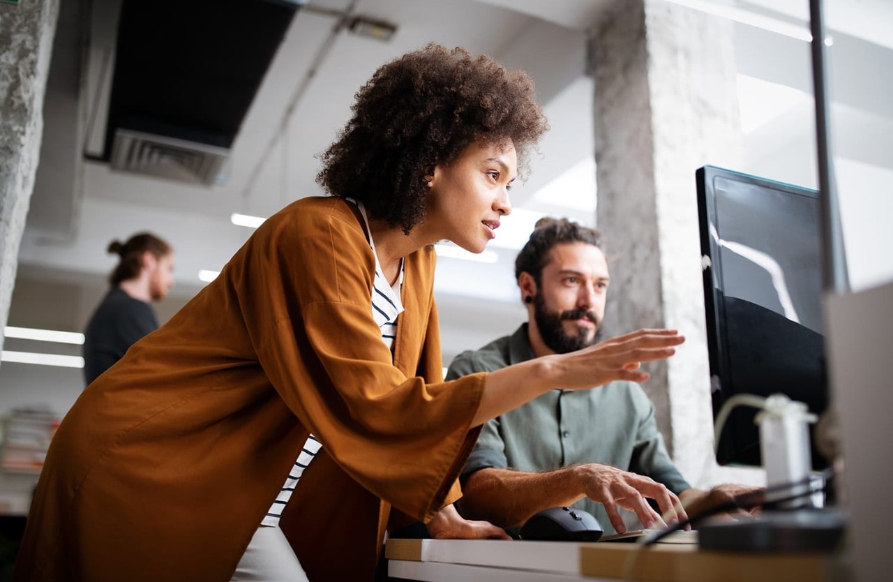 Programmers collaborating on desktop computer in modern office