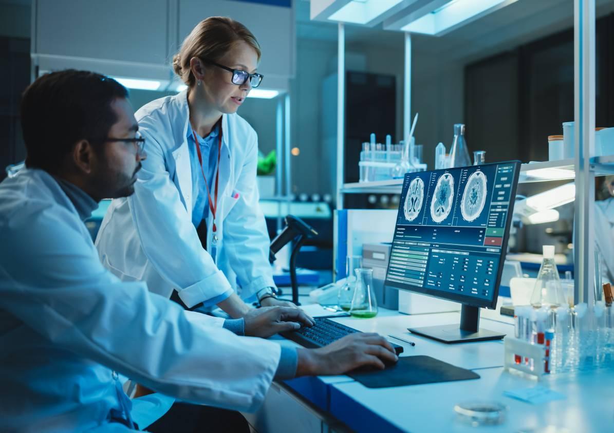 Two health care professionals in lab coats reviewing data on a computer screen