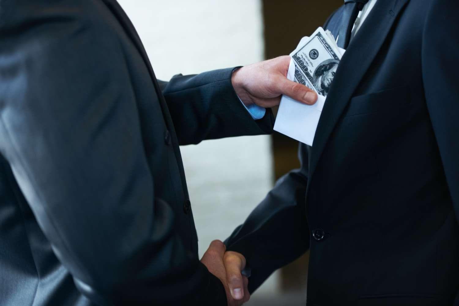 Two corporate businessmen shaking hands while one man places money in the other  