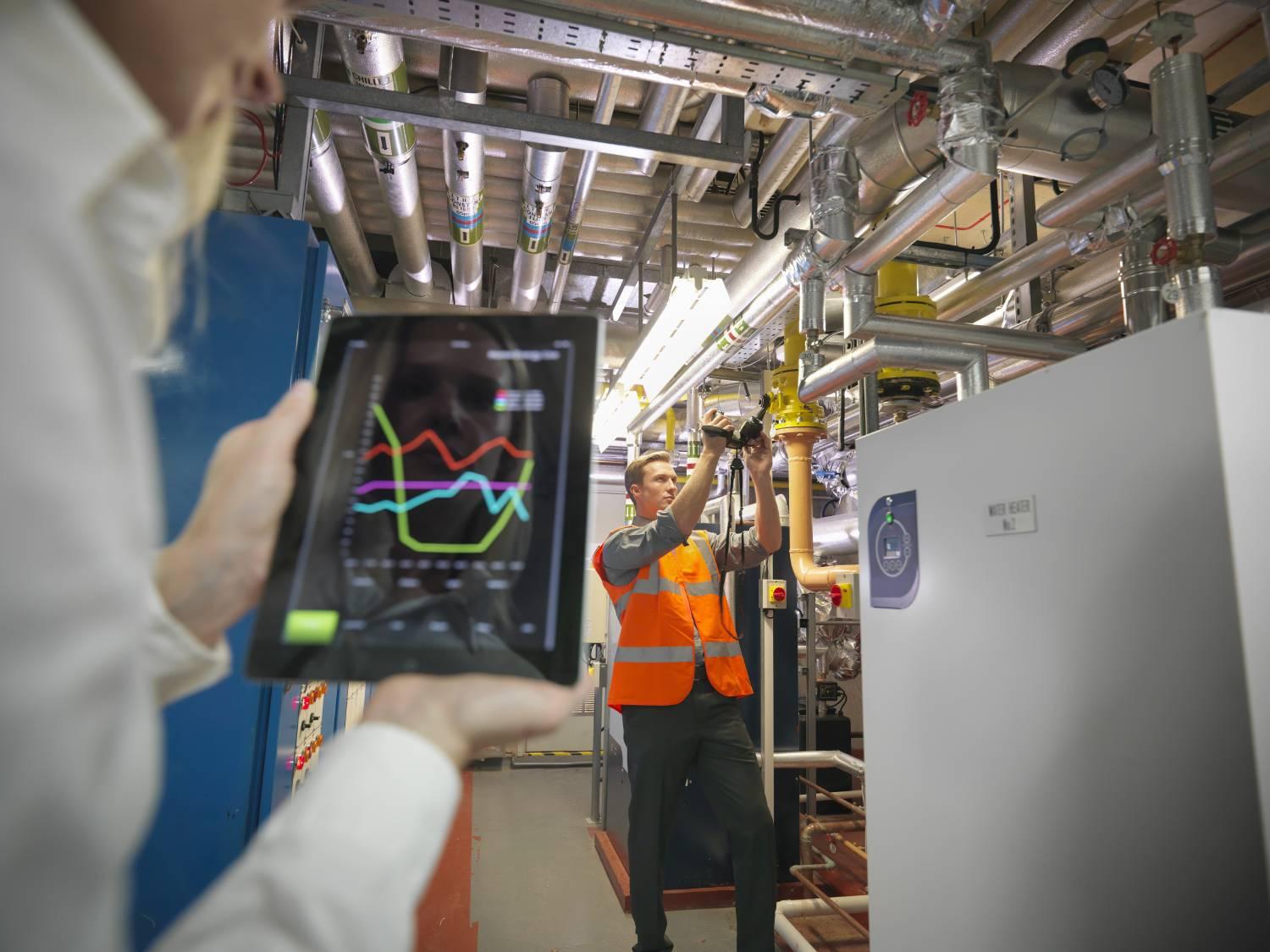 Workers with tablet checking efficiency of heating in boiler room