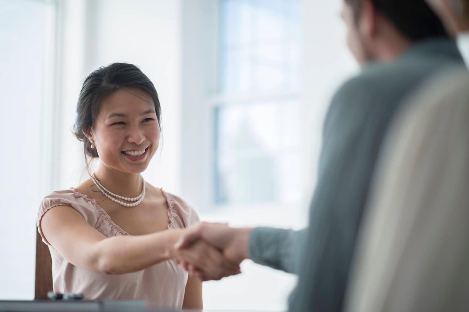 A smiling Asian woman shakes hands with another person
