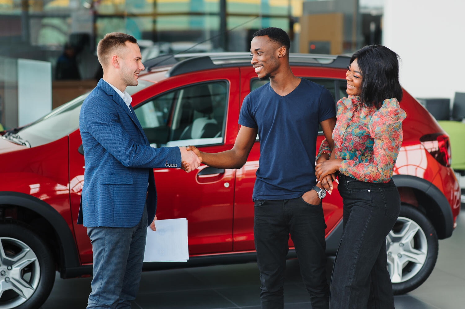 salesman showing new car to african couple in showroom