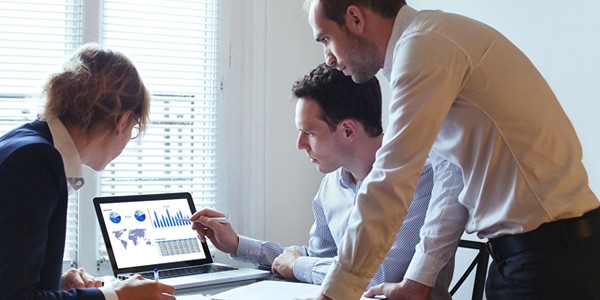 Two men and a woman looking at graphs and charts on a laptop