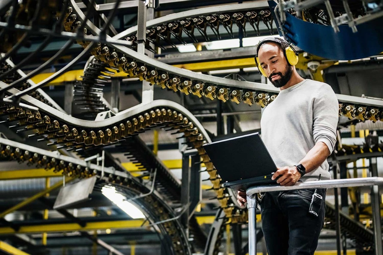 Man looks at laptop in front of factory conveyor belts
