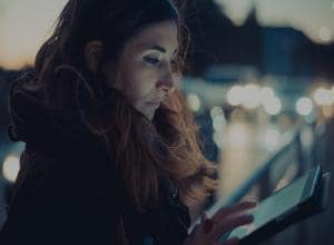 Mid adult woman using digital tablet touchscreen on street at dusk