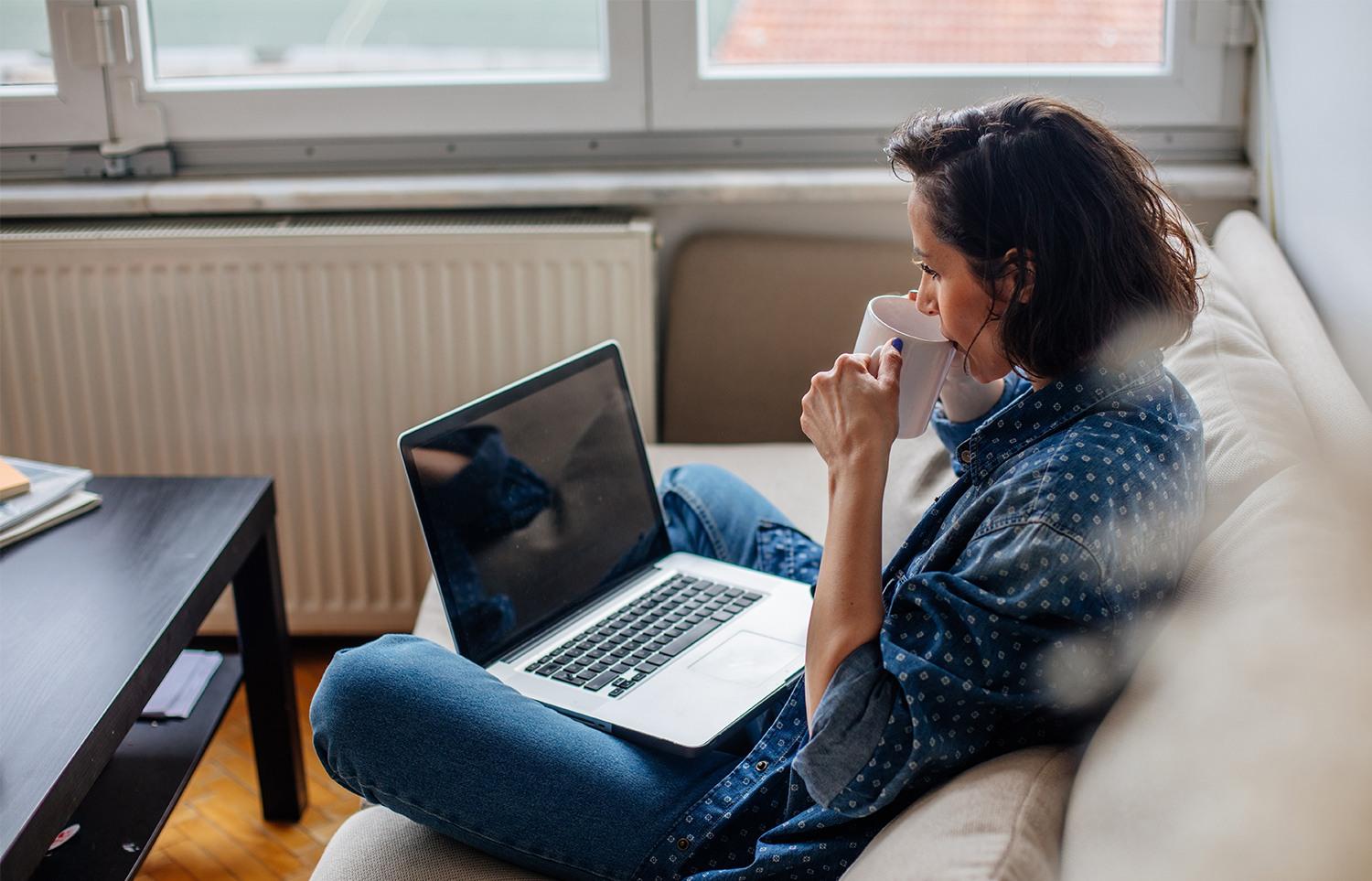 Woman drinking coffee and using a laptop in home