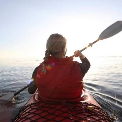 A woman paddles her kayak on a calm sea.