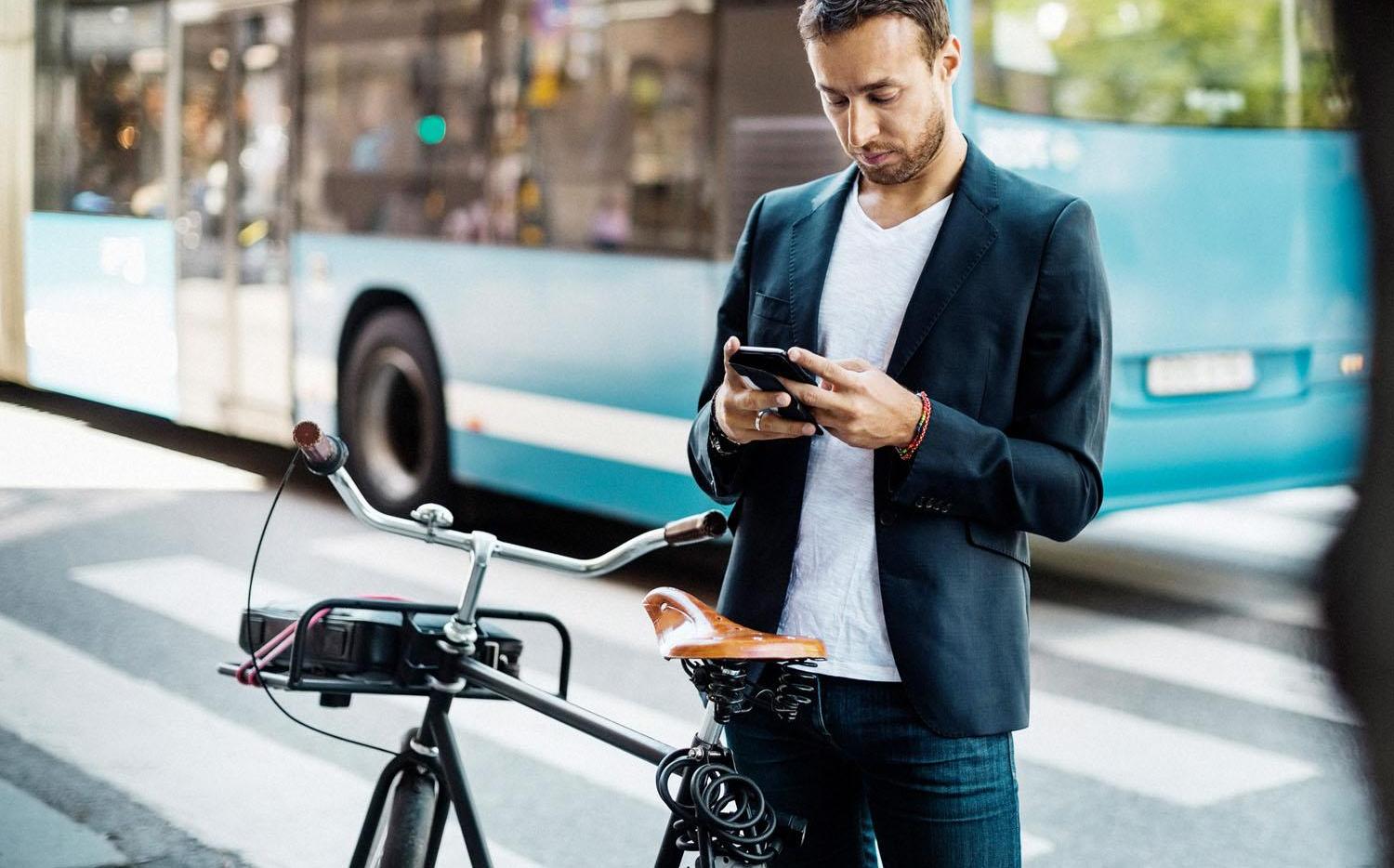 Businessman using mobile phone while standing with bicycle on city street 