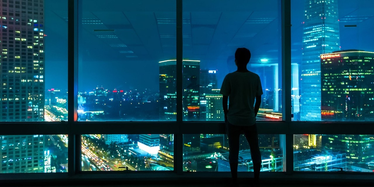Man starring at city through window at night