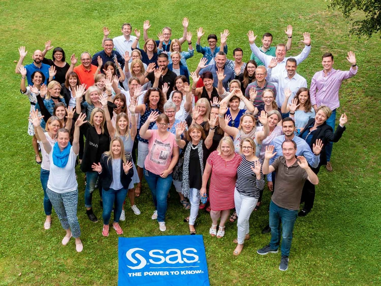Grupo de empleados de SAS en el césped del campus sonriendo y saludando 