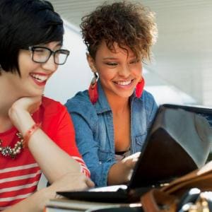 Dos mujeres de negocios miran su laptop y sonríen
