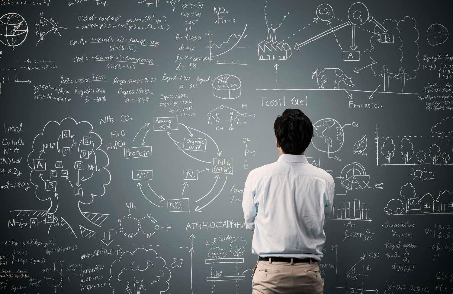 Man with back to camera looking at data and drawings on chalkboard