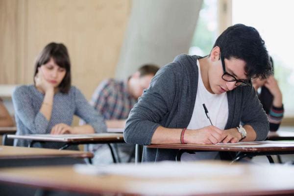 Focused male college student taking test at desk in classroom 
