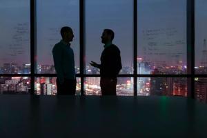 Two men talking at night in office with city view