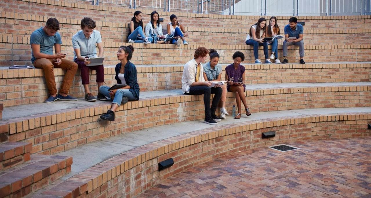 Estudiantes sentados en escalones usando un dispositivo