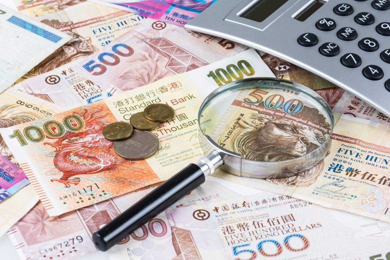 A magnifying glass and a calculator sitting atop a pile of currency