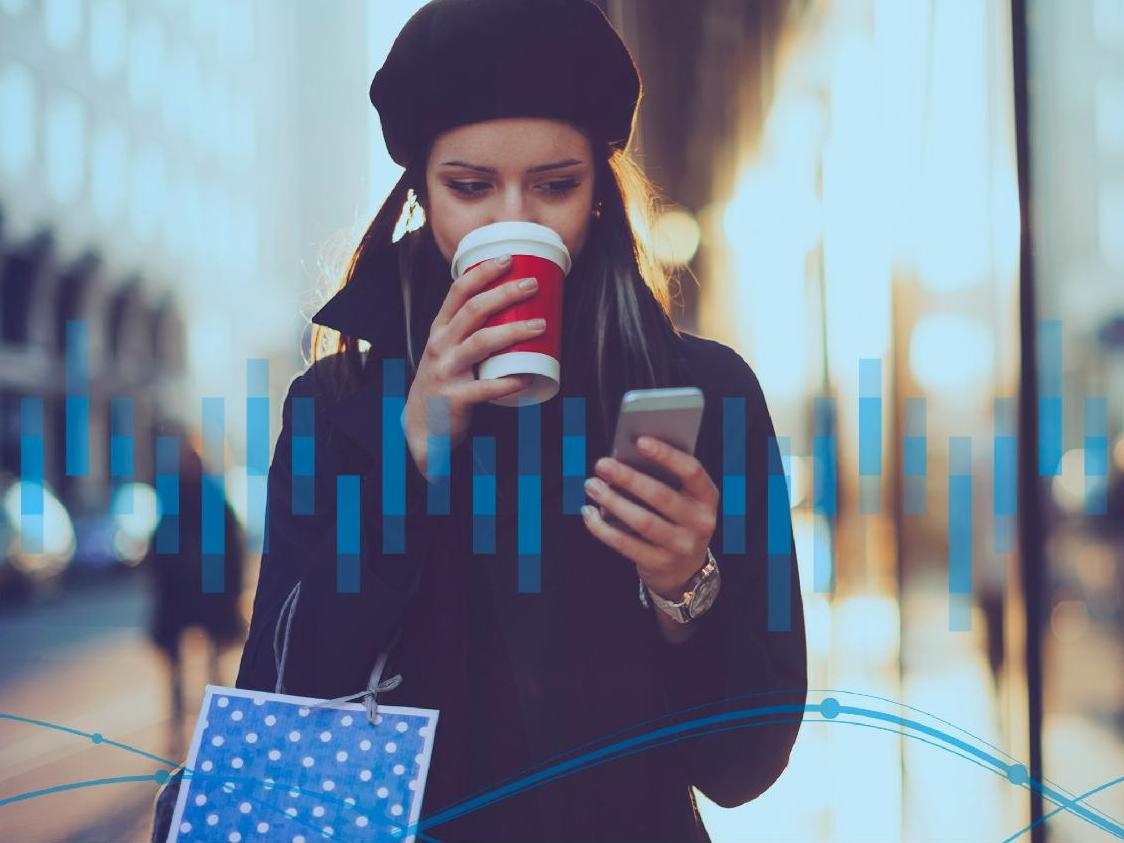 Mujer caminando por la calle con la bolsa de la compra y el teléfono en la mano