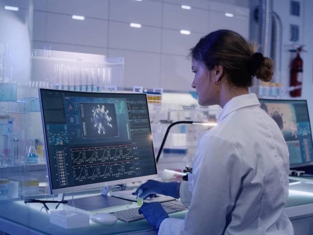 Mujer con bata de laboratorio revisando datos de salud en una computadora pantalla