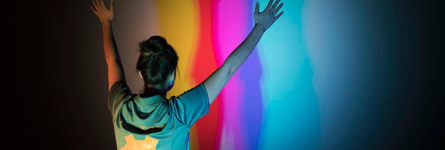 Young woman reaching arms into air in front of a colorful wall