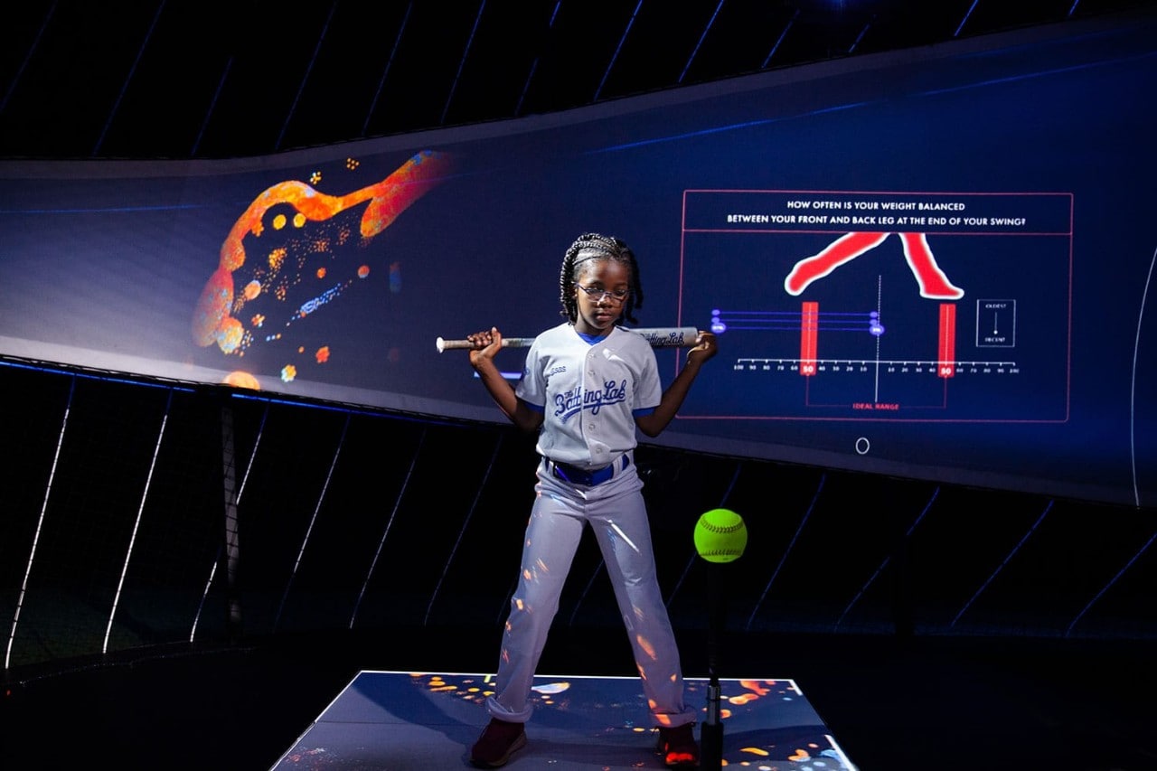 Young girl comes to bat in a simulated batting cage that tracks performance through analytics