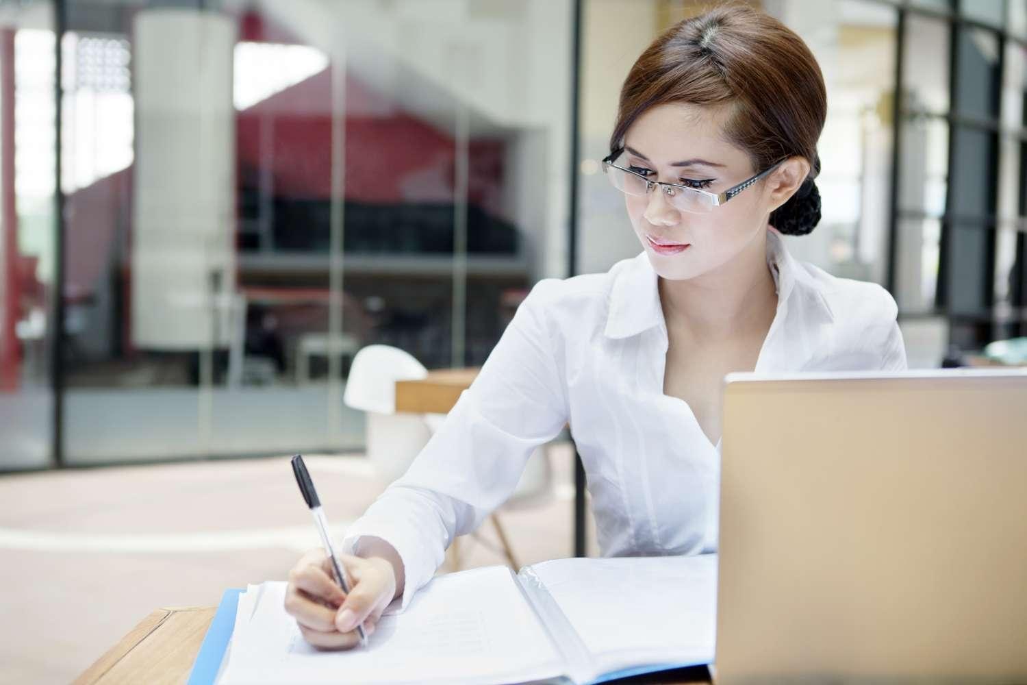 Business woman in office setting at laptop with notepad
