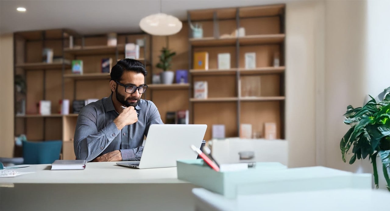 Un homme indien portant des lunettes utilise un ordinateur portable dans un bureau moderne