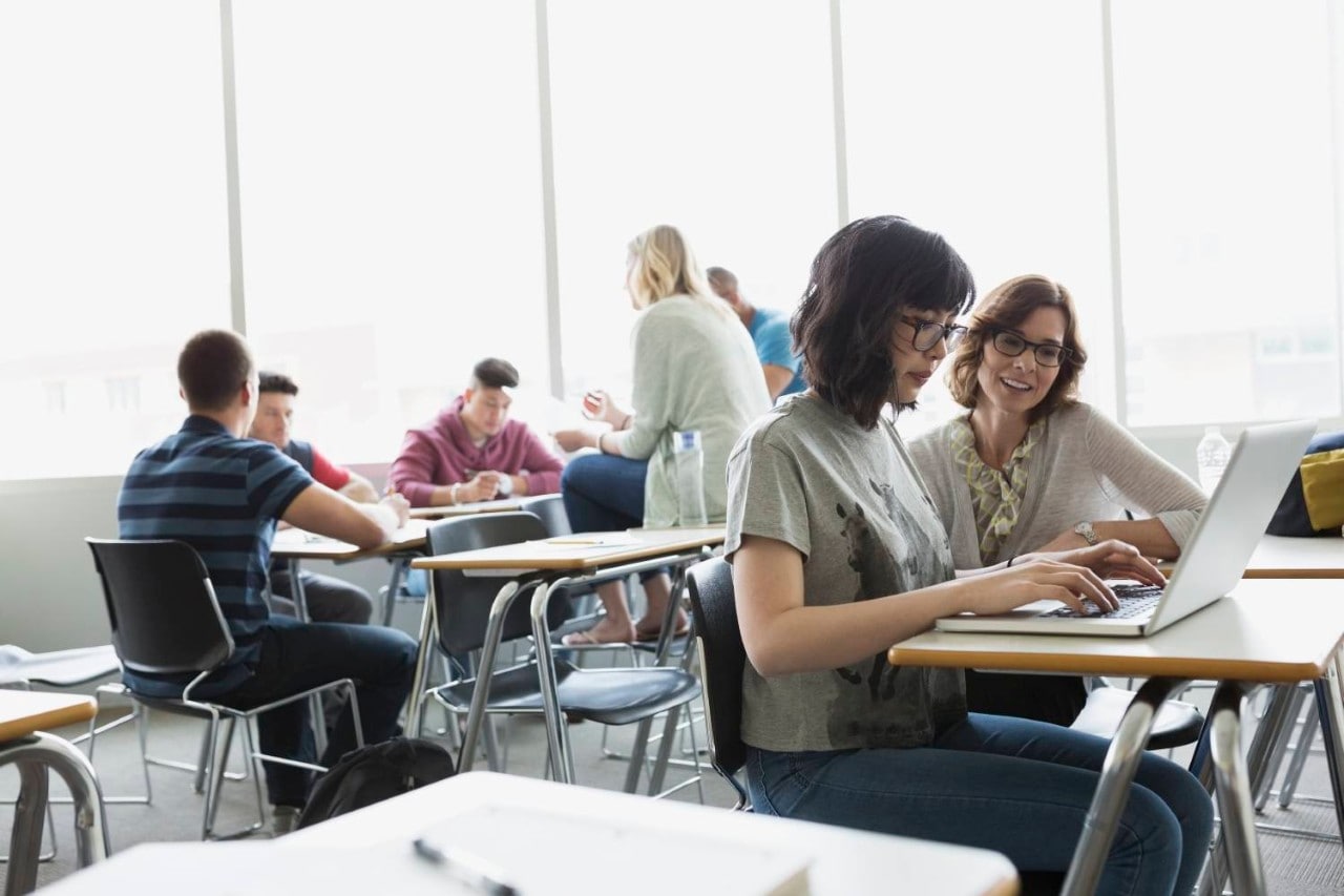 Un professeur aide un étudiant à utiliser un ordinateur portable dans une salle de classe.