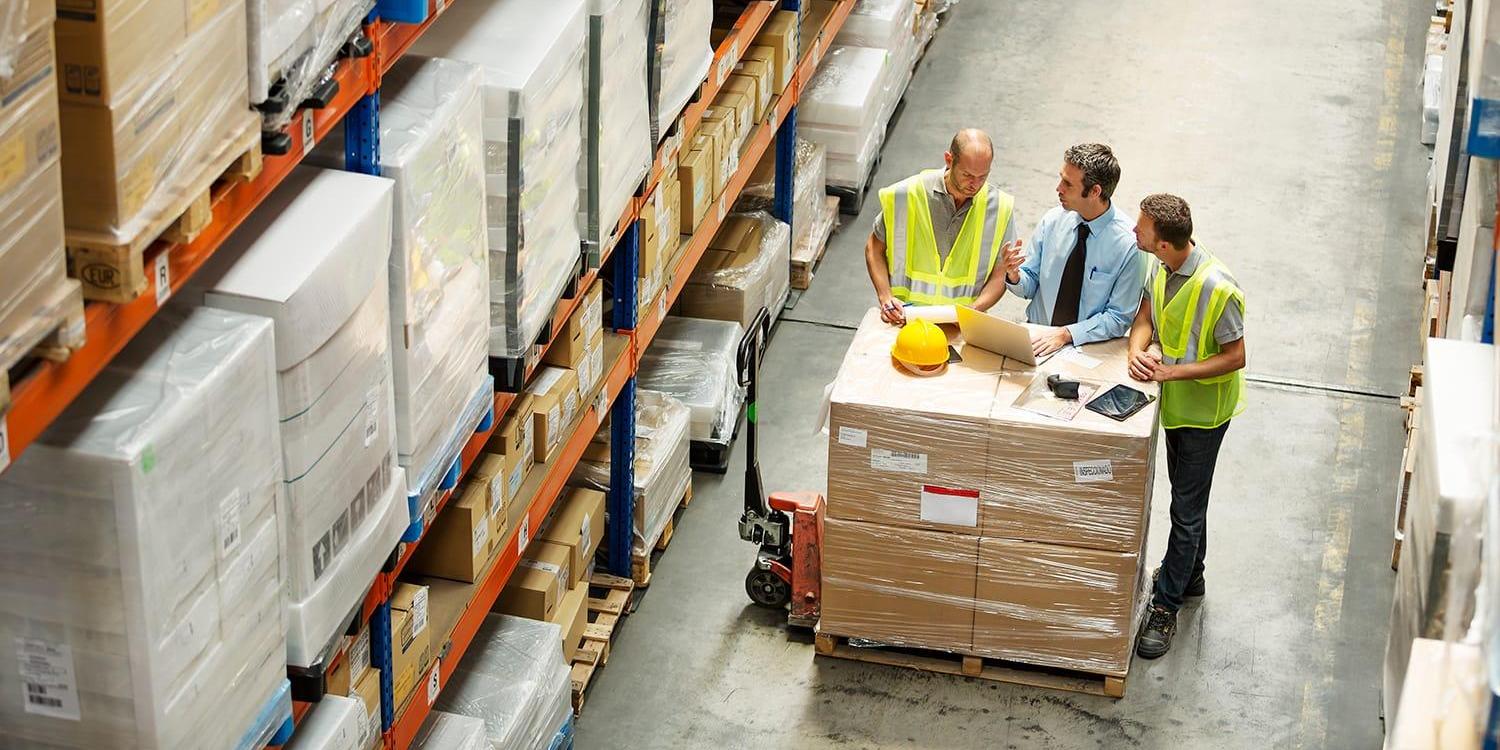 Three workers in warehouse setting around laptop computer