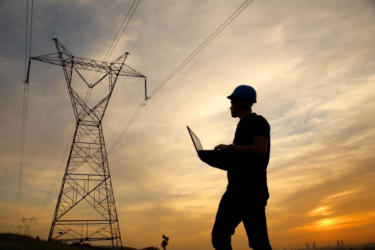 Power gird worker with tower in the background at sunset